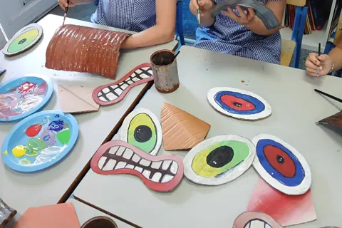 Children painting cardboard mask pieces at a table