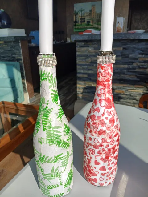 Two decorated candle-holder bottles with green fern and red floral patterns
