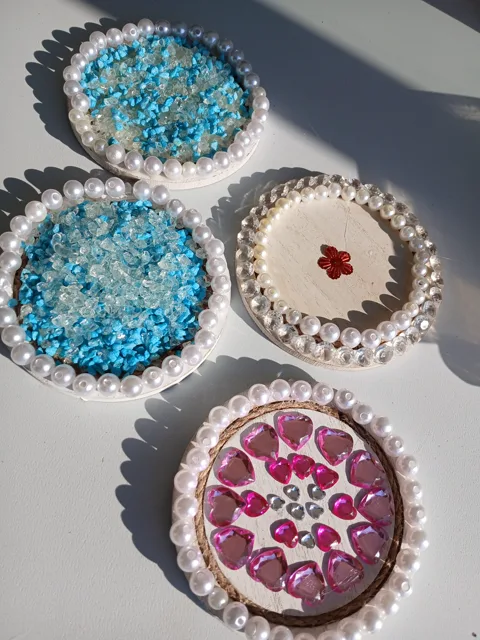 Four wooden coasters decorated with blue gems, pink hearts and white pearls