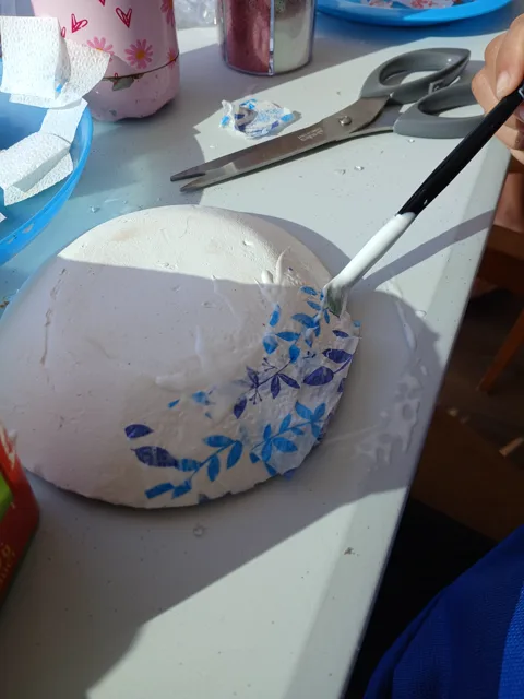 Blue-patterned paper bowl craft beside scissors and tissue paper