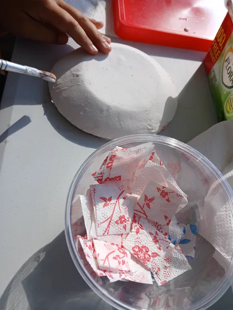 Hands applying glue to a white paper bowl during an art session