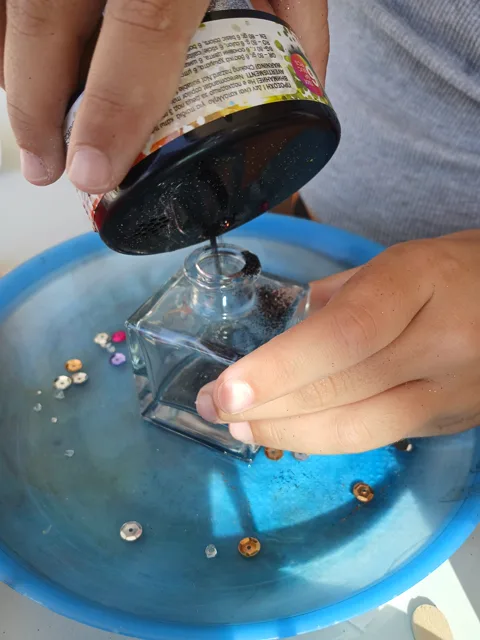 Hands pouring decorative stones into a glass jar