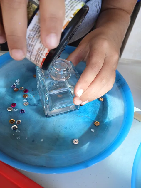 Hands decorating a small glass jar with beads and colourful gems