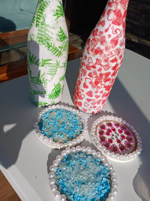 Patterned candle-holder bottles and pearl-edged gem coasters displayed together