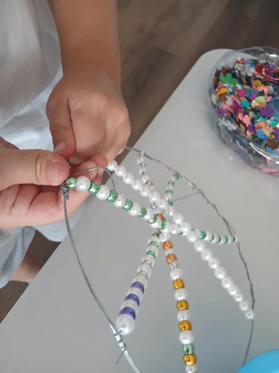 Hands threading pastel beads across a dreamcatcher wire frame